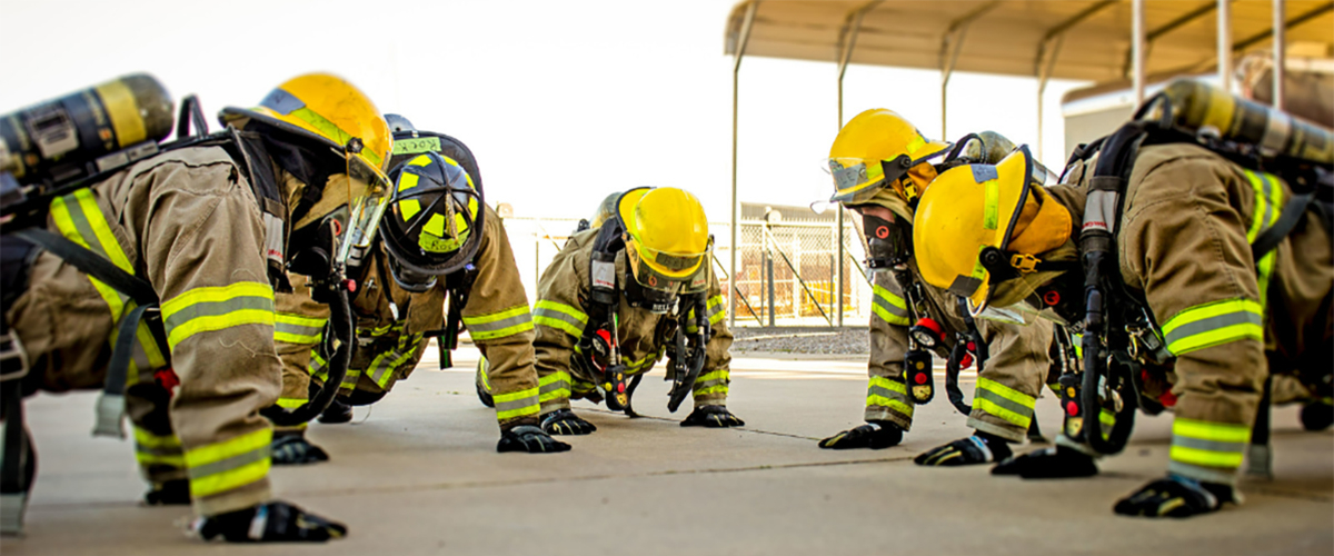 Firefighters doing pushups in full gear.