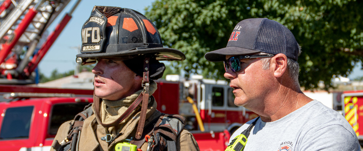 2 firemen talking at the scene of a fire.